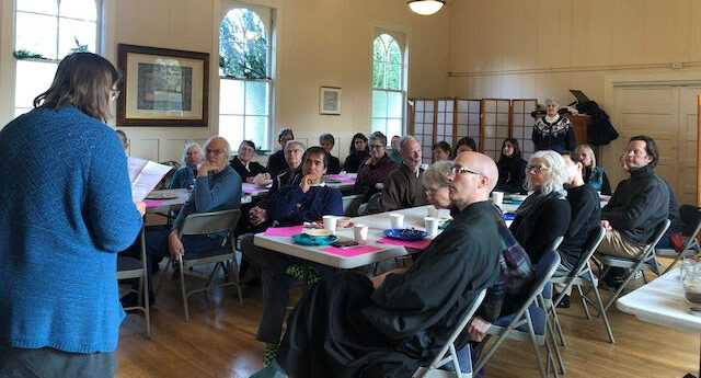 people sitting at tables listing to a committee report at a sangha meeting.