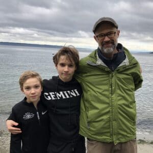 Josh with his two sons standing in front of water on a cloudy day.