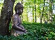 a Buddha in meditation posture sitting under a tree in a field of ivy.