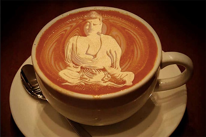 A cup of coffee with a Buddha image in the foam