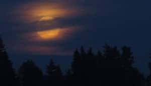 Night sky with orange moon obscured by clouds.