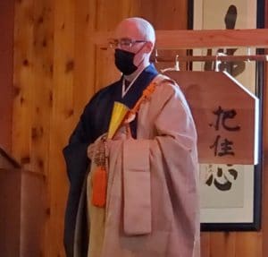 Abbot Koshin in ceremonial robes standing in front of the han.