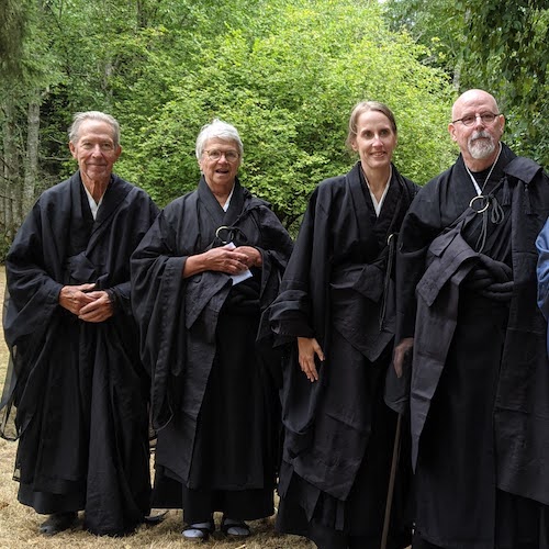 Our four ordained lay monks wearing black robes with greenery behind them.