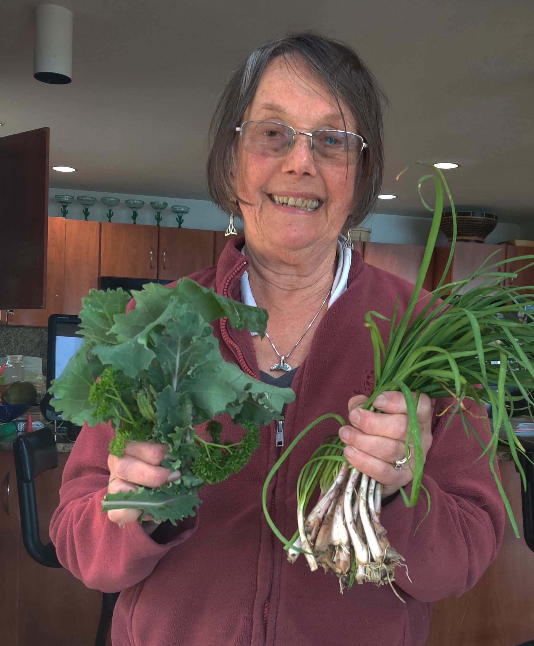 Jean smiling and holding onions and kale from her garden.