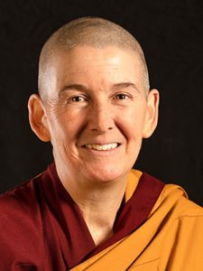 portrait of Tenzin Dasel, smiling, wearing red and orange Tibetan Buddhist robes