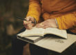 Arms and hands of a person wearing orange robes, holding a pen and notebook, ready to write.
