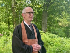 Eko Jeff Kelley standing in front of green bushes and trees in the Zen Center garden.